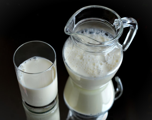 Caraffa e bicchiere di latte su sfondo nero.